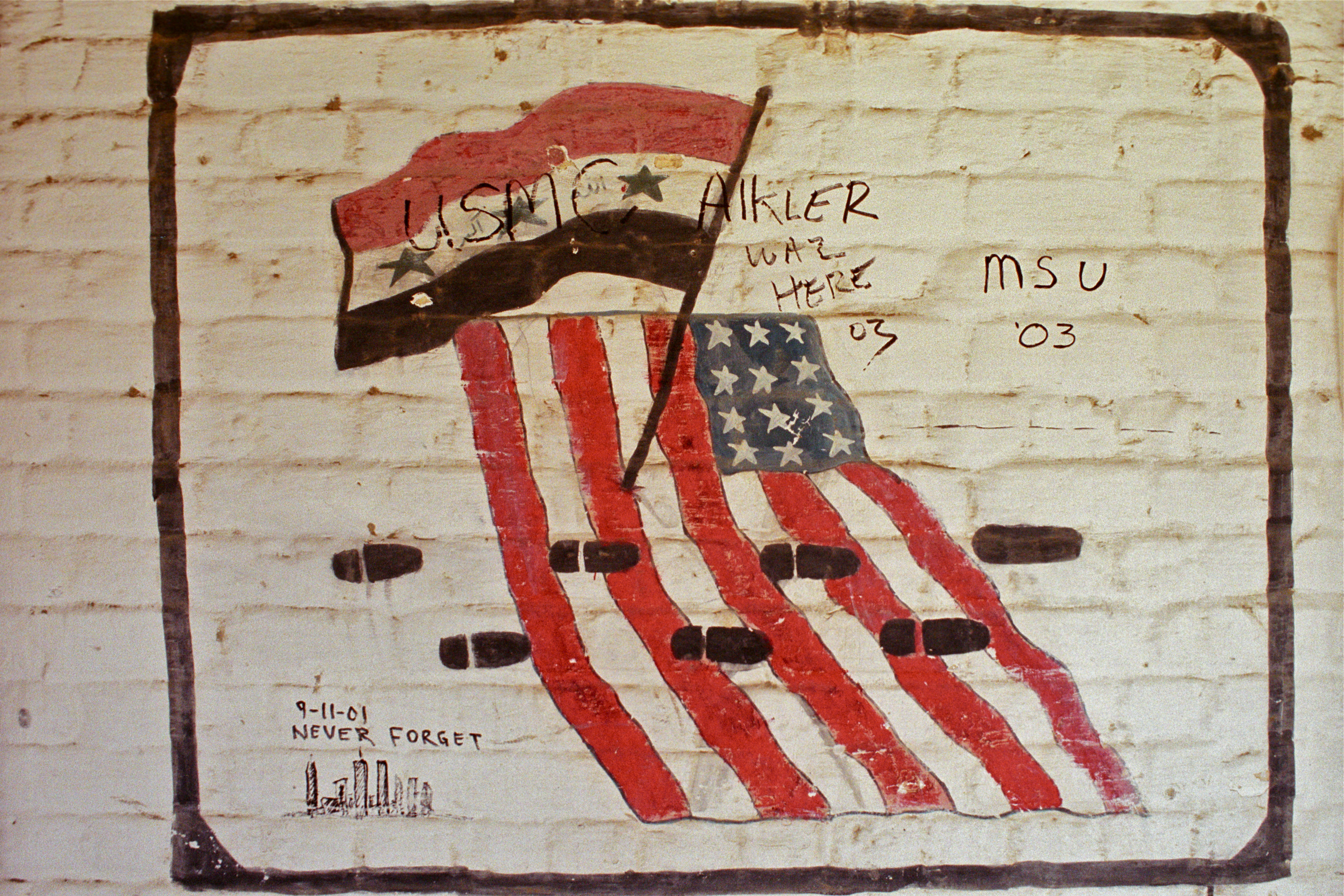 Graffiti from a Marine unit on an abandoned Iraqi military barracks shows the Iraqi and American flags in 2003. Photo taken by Benjamin Busch.